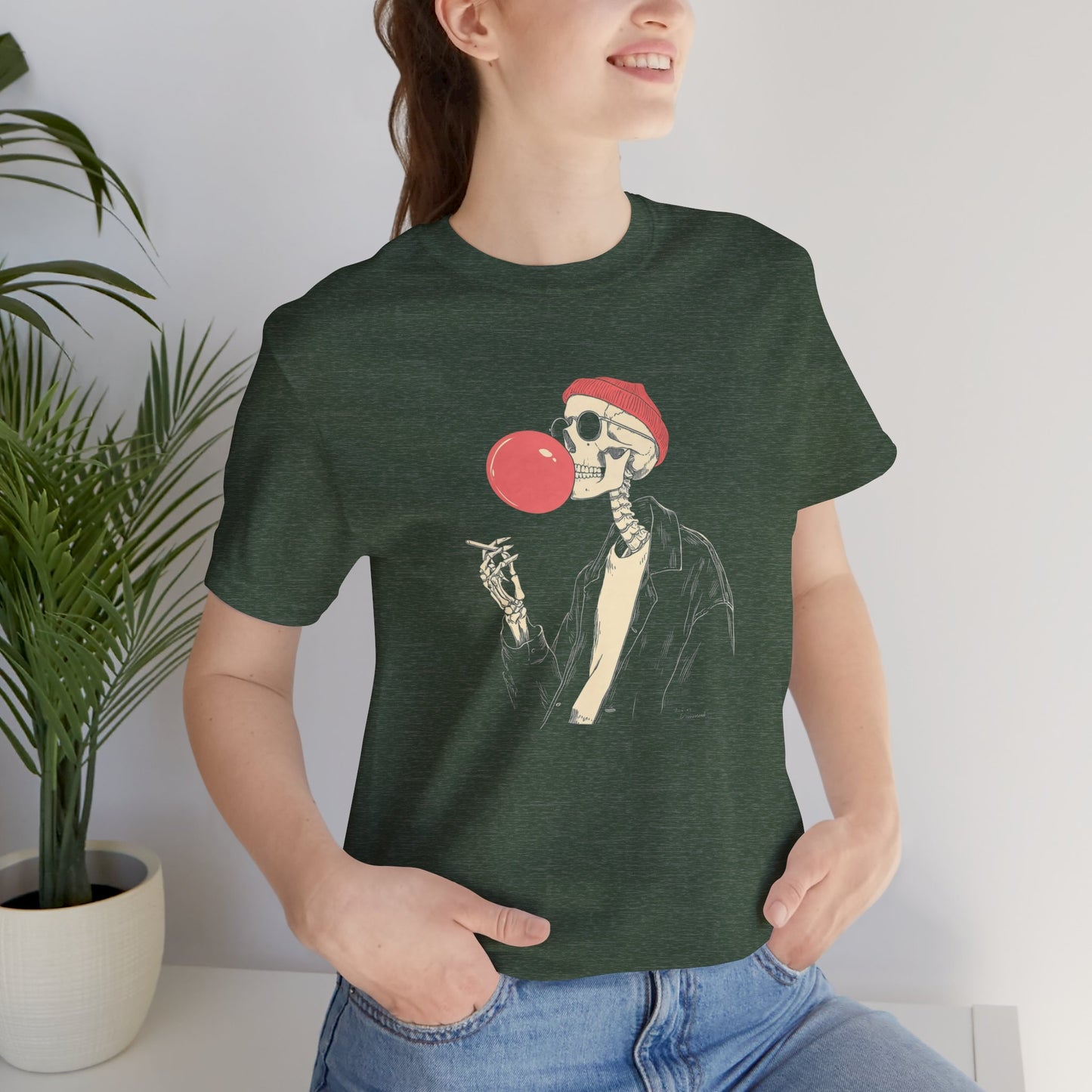 Person wearing a green t-shirt with a skeleton design blowing a red bubblegum bubble.