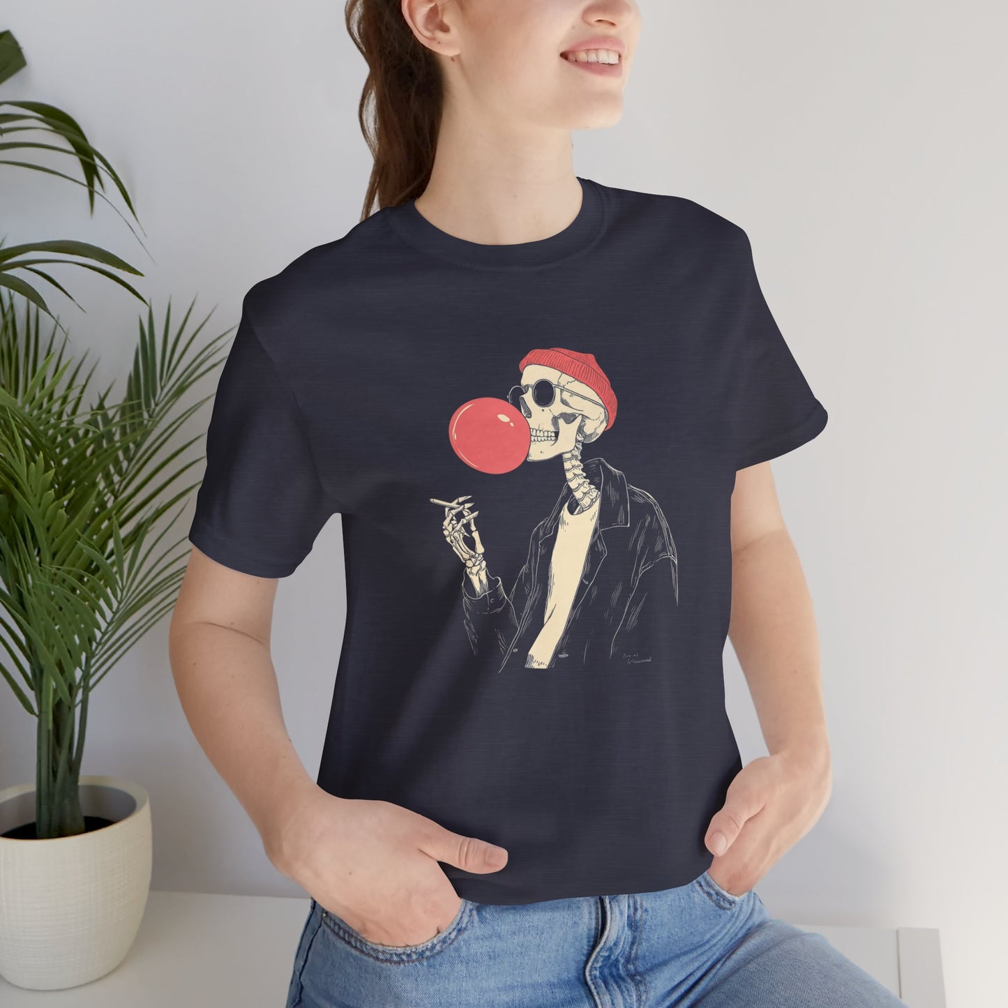 Person wearing a black t-shirt with a skeleton design blowing a red bubblegum bubble.