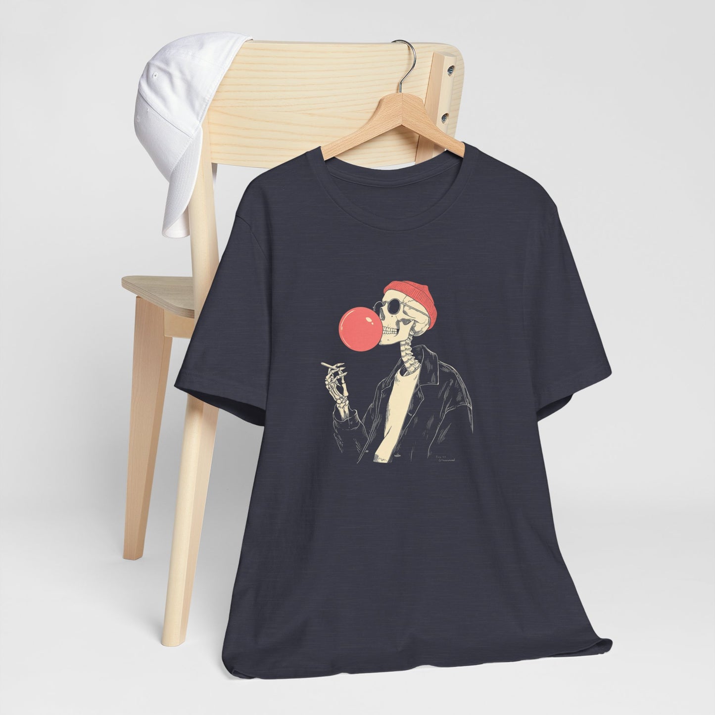 Black t-shirt with a skeleton design blowing a red bubblegum bubble, hanging on a wooden chair.
