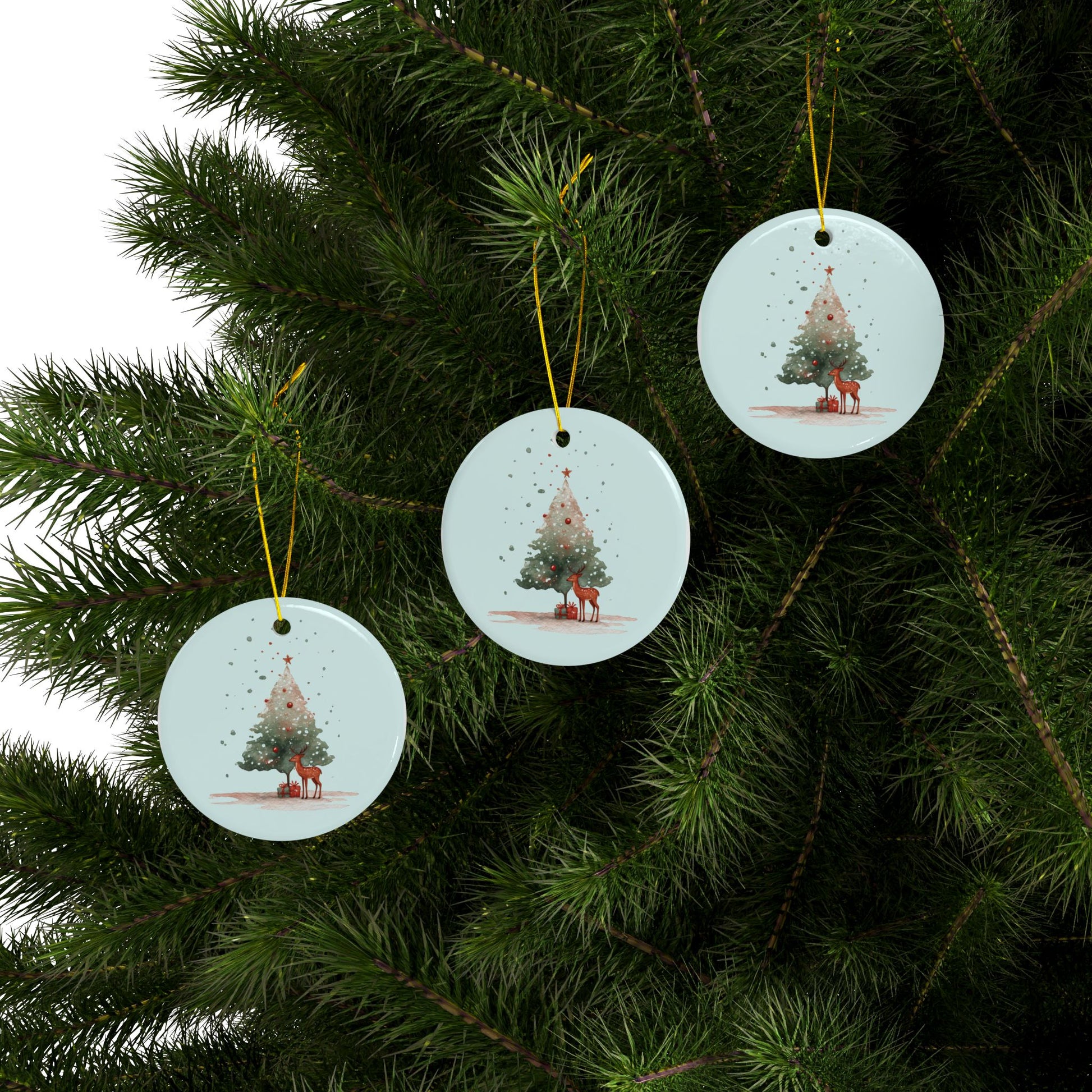 Three Christmas tree ornaments with reindeer designs hanging on a green pine branch.