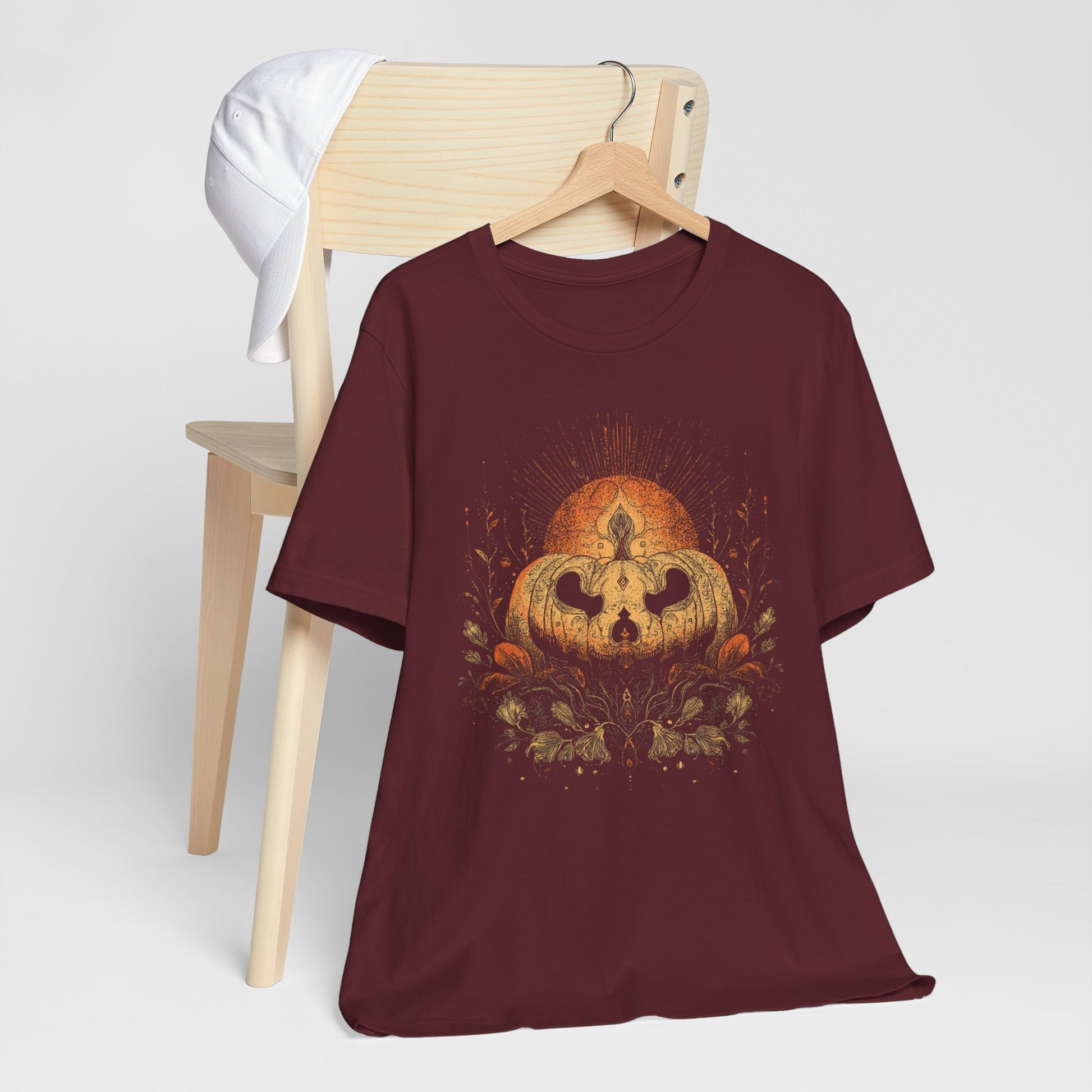Maroon t-shirt with pumpkin design on a wooden chair against a white background