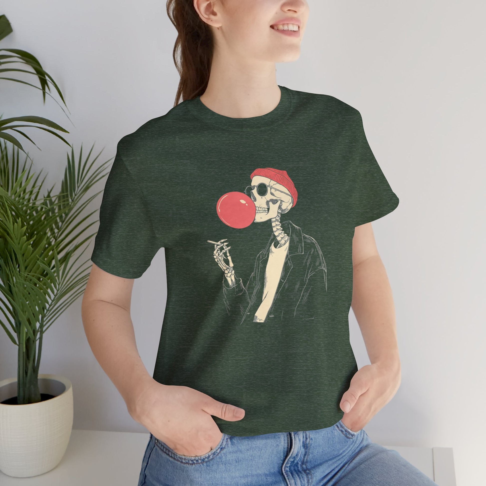 Person wearing a green t-shirt with a skeleton design blowing a red bubblegum bubble.