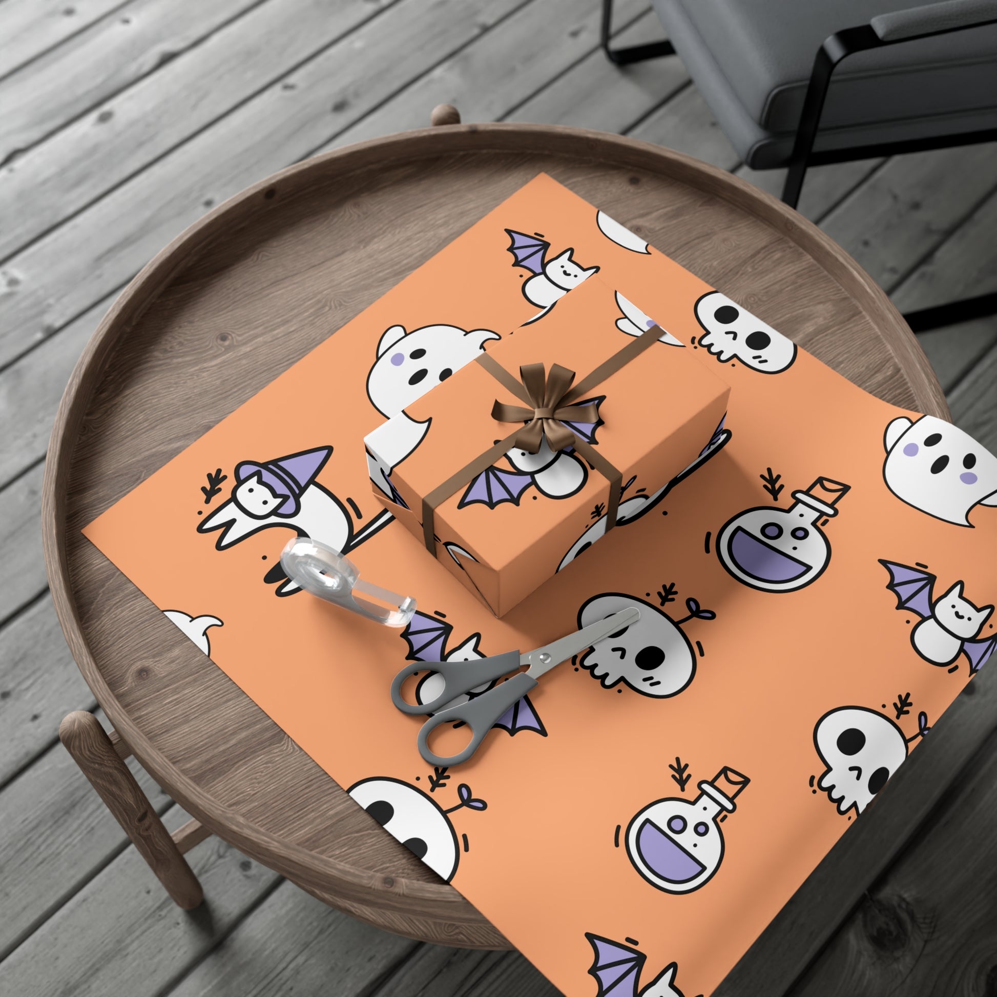 Gift box on an orange Halloween-themed placemat with ghosts, bats, and potion bottles on a wooden surface.