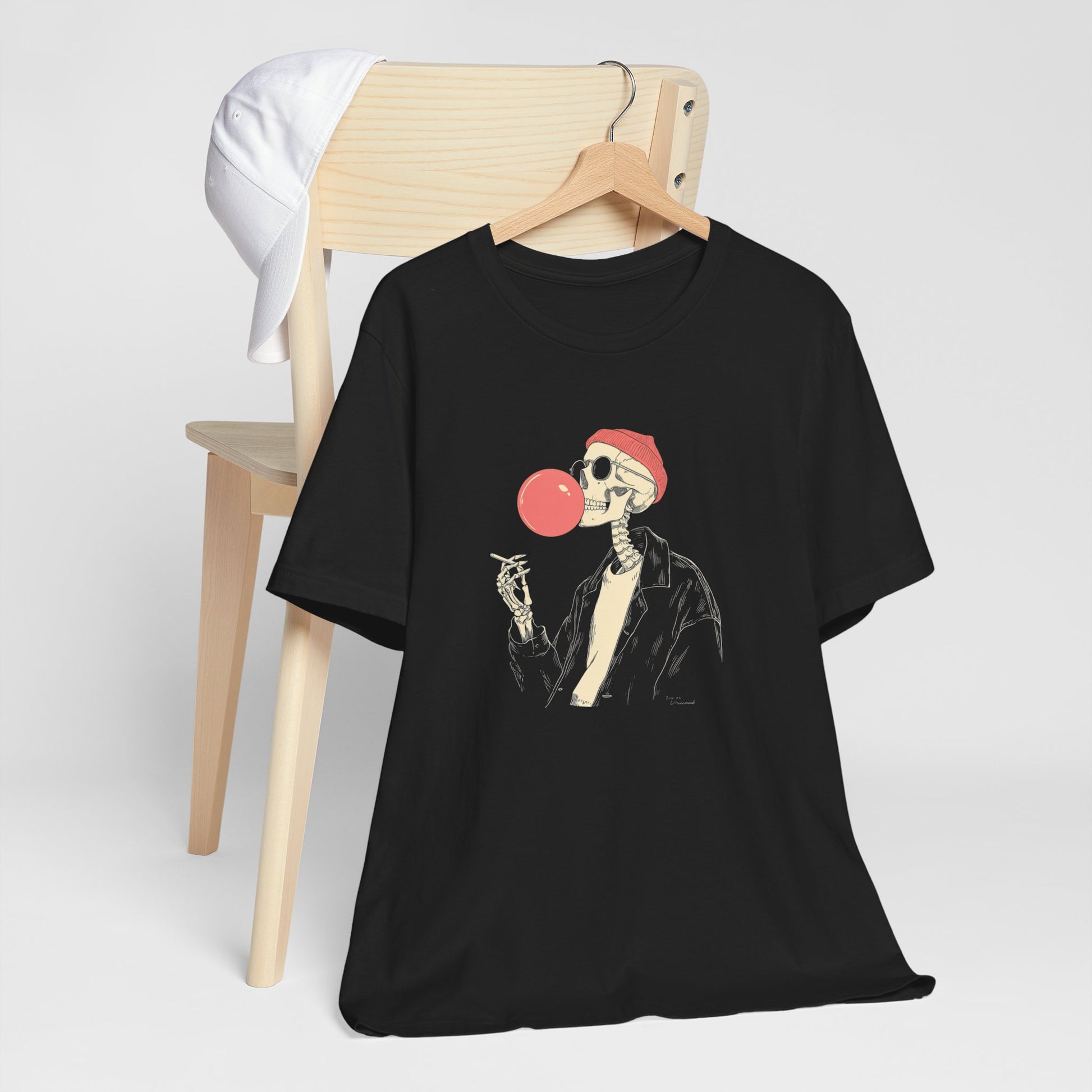Black t-shirt with a skeleton design blowing a red bubble gum bubble, hanging on a wooden chair.