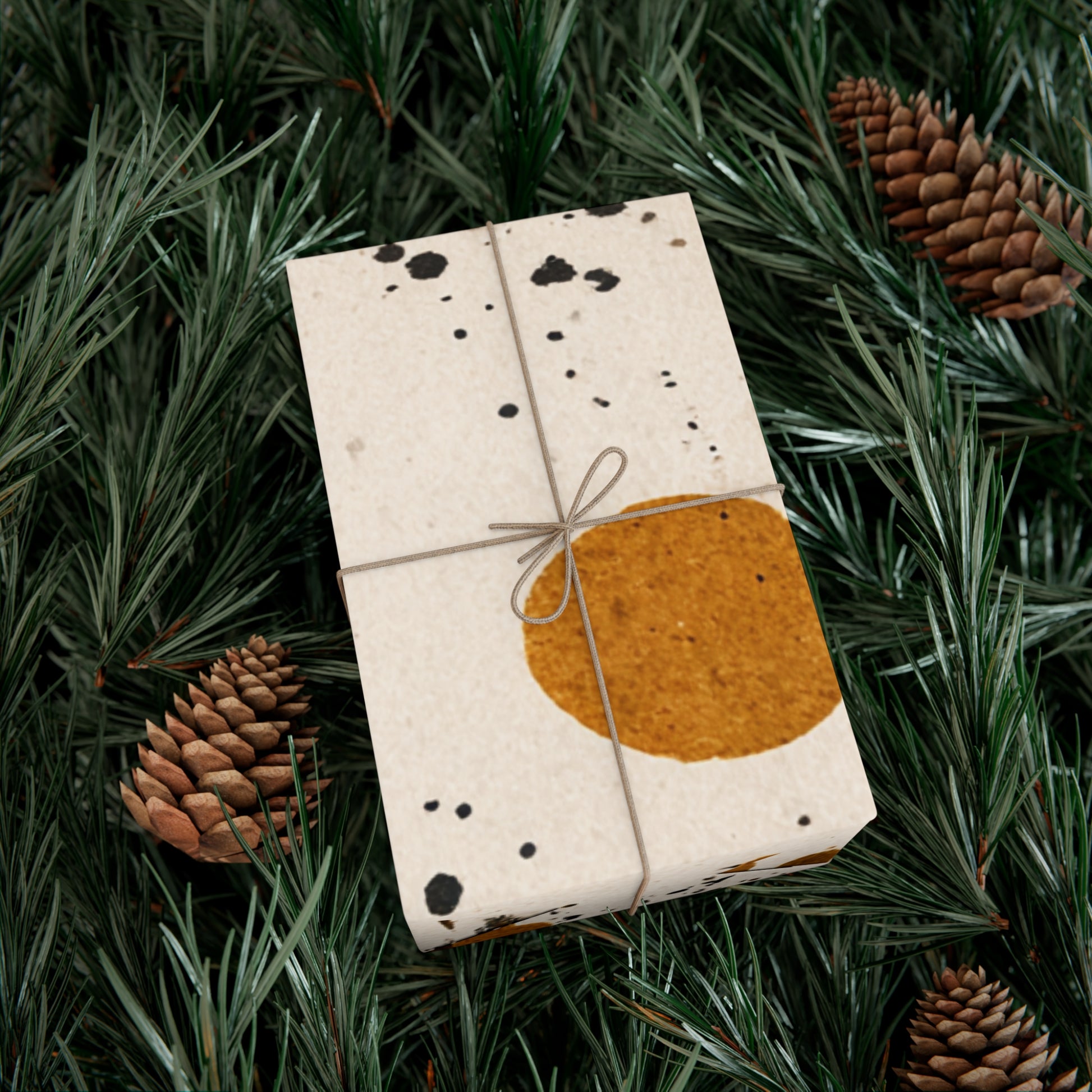 Gift box wrapped in paper with a brown square design, tied with string, on green foliage with pine cones.
