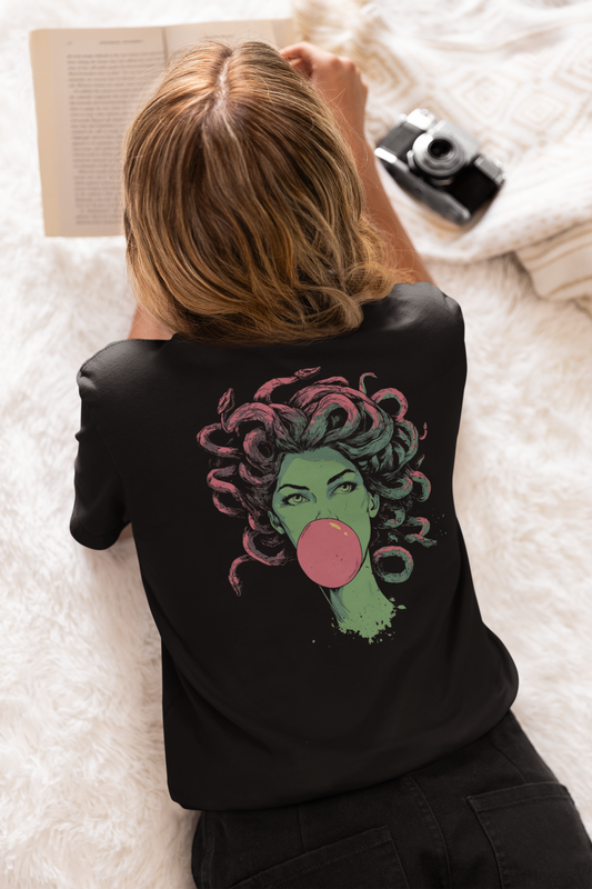Person wearing a black t-shirt with a colorful graphic design, lying on a white blanket with books and a camera.